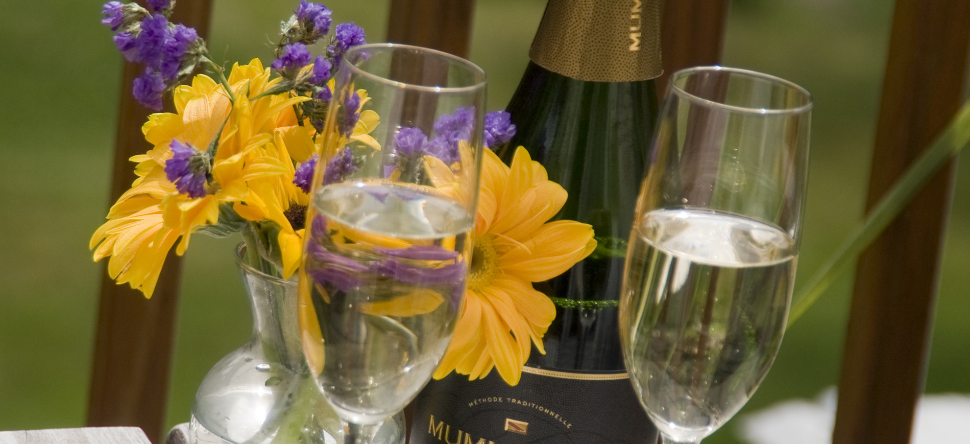 champagne glasses in front of vase of yellow and purple flowers and champagne bottle