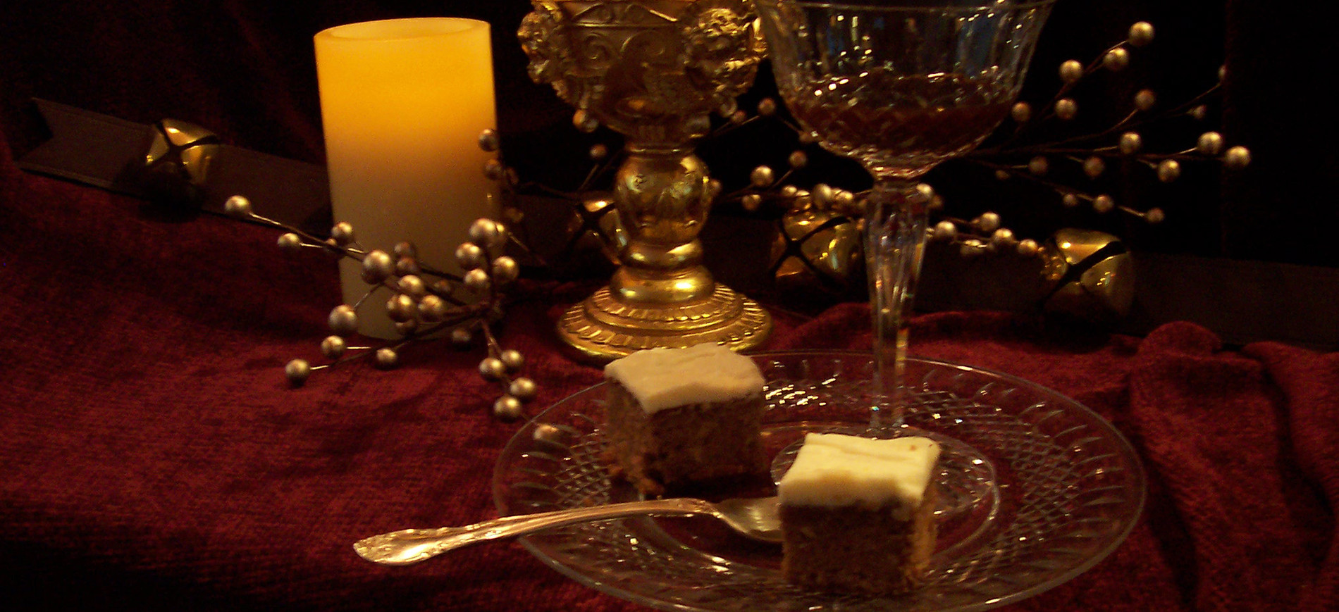 Burgundy velvet cloth with pillar candle, gold goblet, champagne coupe, lebkuchen brownies on glass plate with fork