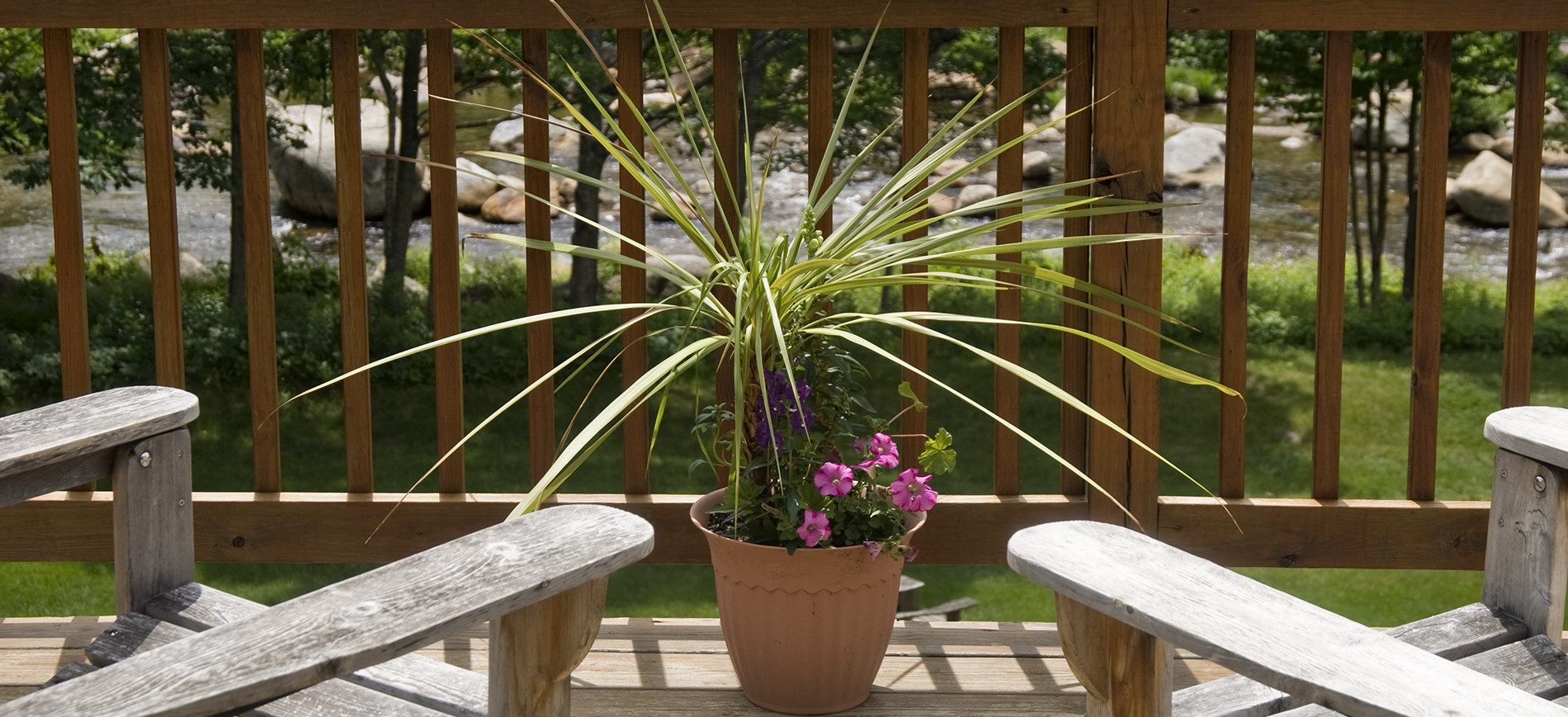 balcony overlooking river with arms of two chairs & pot of flowers between them