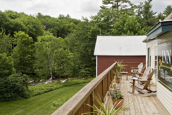 Lawn along Ellis River, red barn, wood balcony with plants & Adirondack chairs