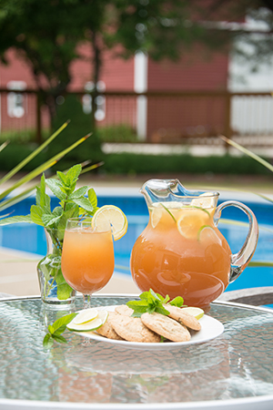 Iced tea pitcher and glasses with plate of cookies on glass table, pool in background