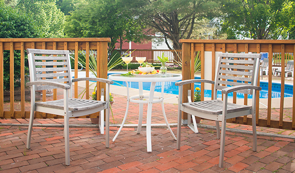 Brick patio with two chairs & table, fence, pool, trees in background