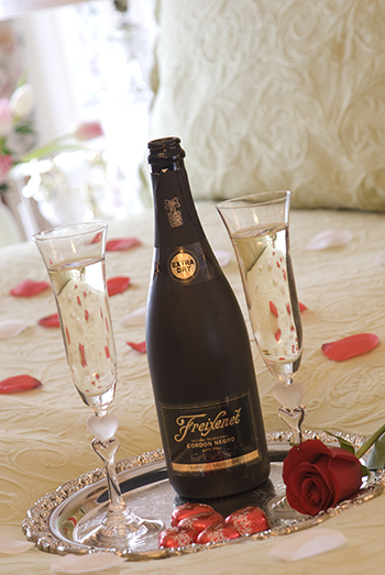 bottle of sparkling wine, two glasses, rost  on bed with rose petals