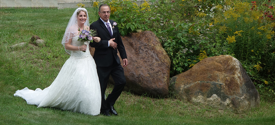 Bride and father walking beside garden