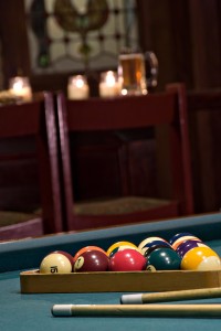 Pool cues & racked balls on pool table with barstools & bar in background